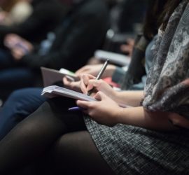 people seated in lecture hall with notebooks on laps