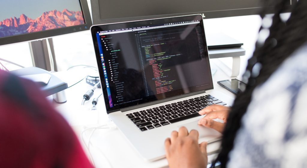 Image of a person's hand typing on a laptop, presumably writing computer code.