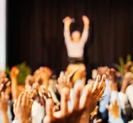 Image of raised hands in a large conference room
