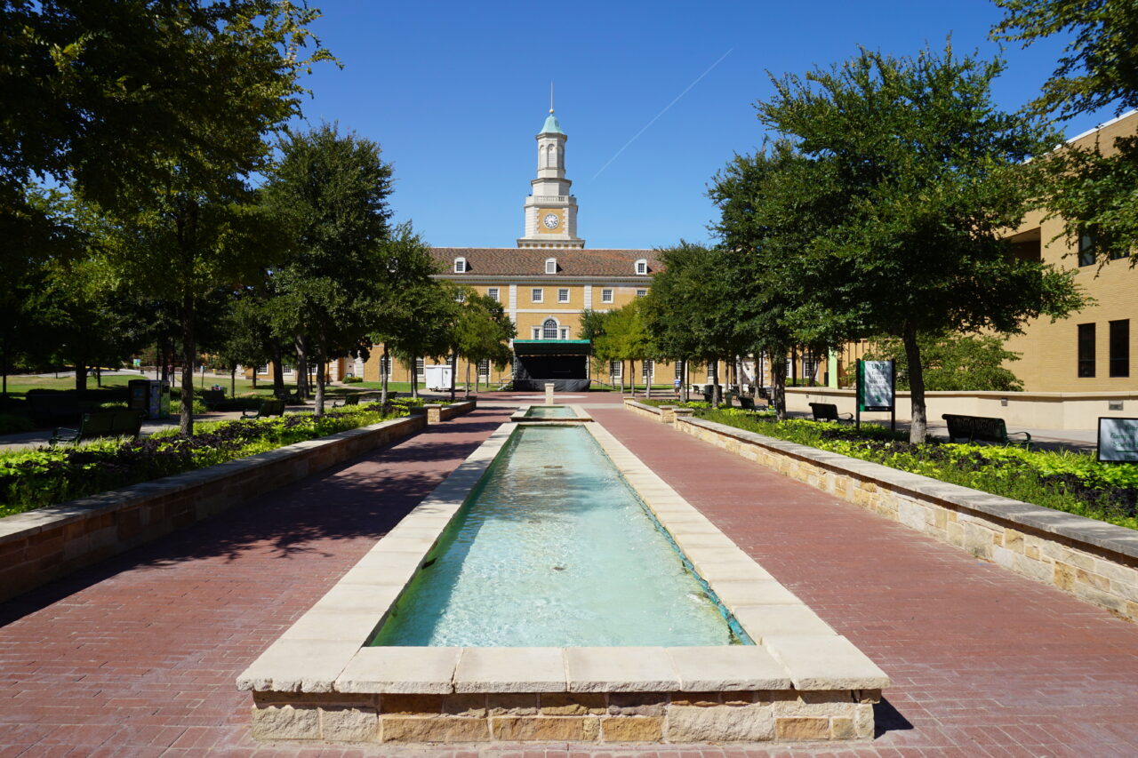 A large yellow brick building at the University of North Texas with water features in front