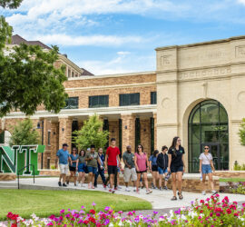 A photo of the outside of University of North Texas new Welcome Center, with a large group of students walking by
